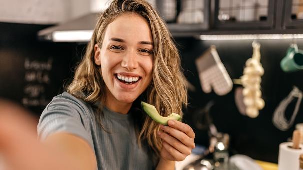 
		Woman smiles at camera and eats avocado
	